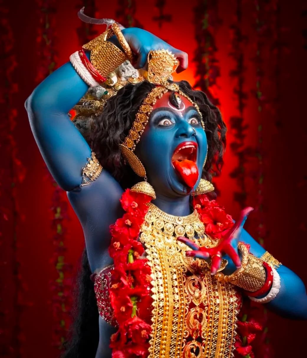 Fierce Goddess Kali in blue form wearing golden ornaments and red flower garland.